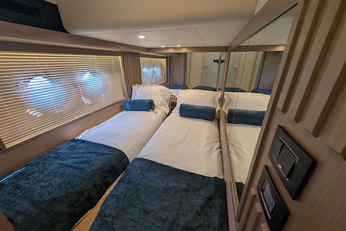 Stylish cabin interior featuring two single beds with blue bedding, mirrors, and large windows with blinds.